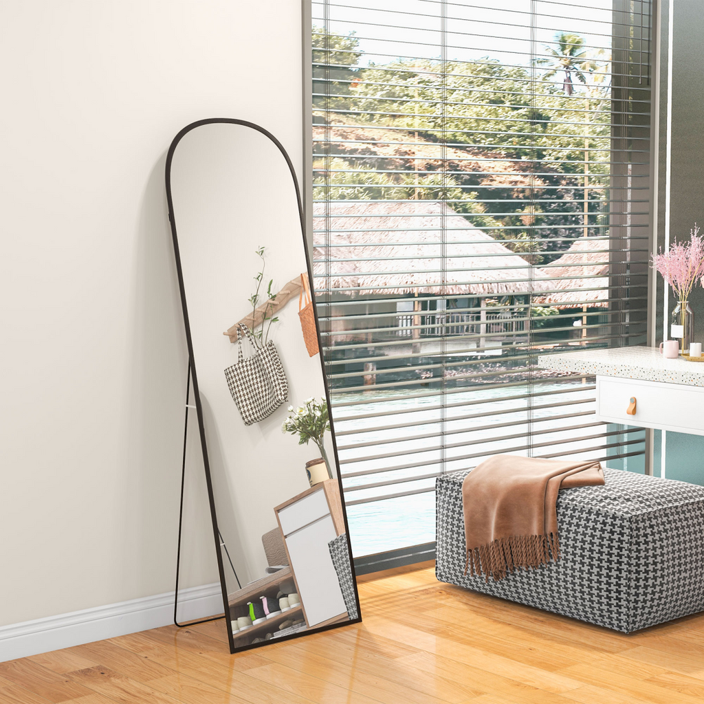 Arched black floor mirror styled beside a bright window