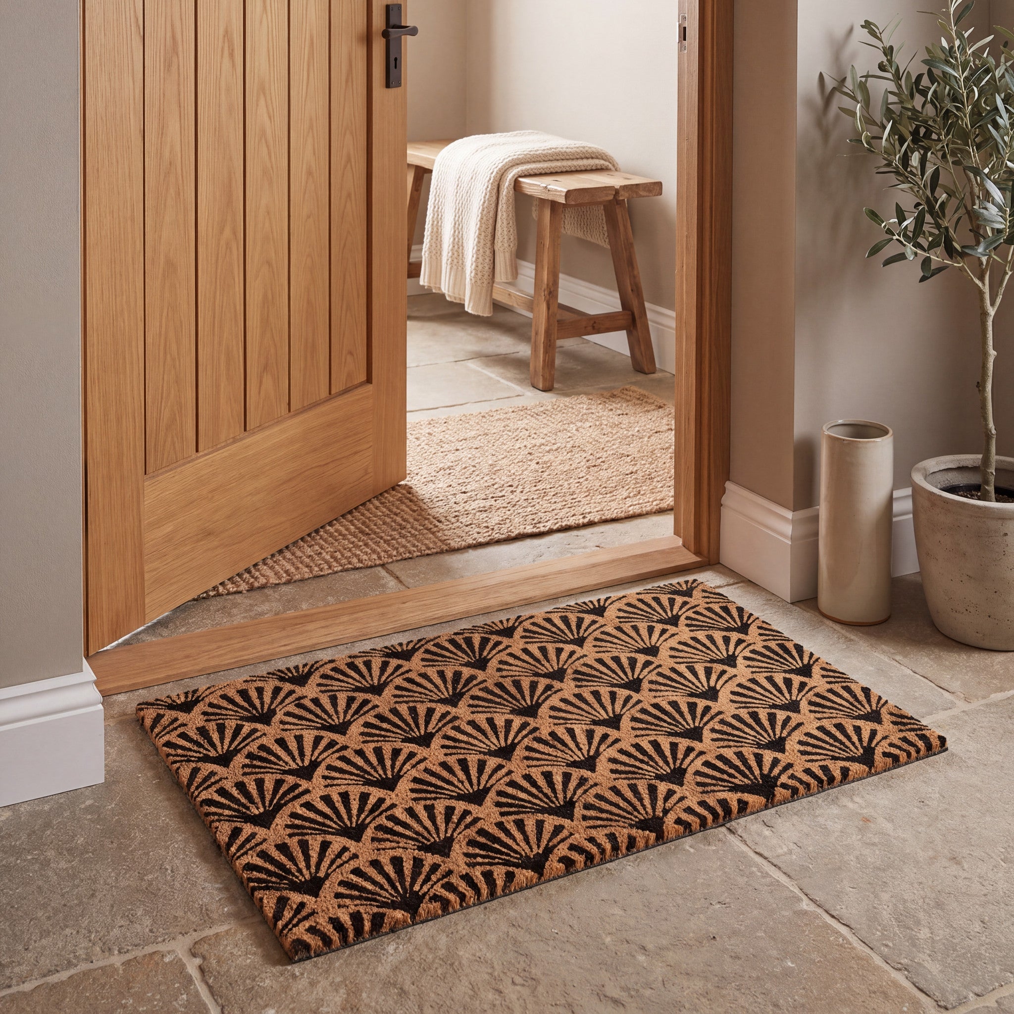 Coir entrance mat with black scallop pattern in a warm natural hallway