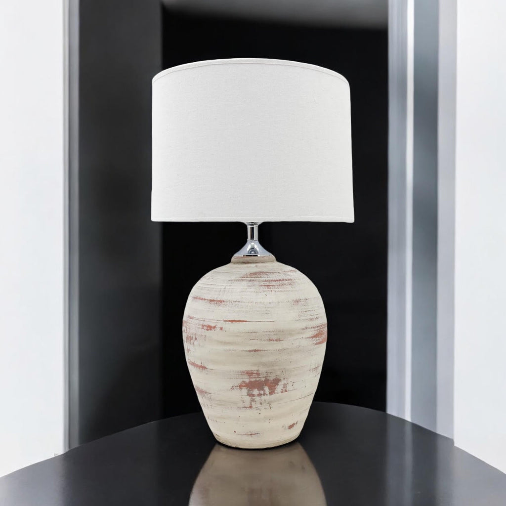 Cream ceramic table lamp with white drum shade on a dark side table