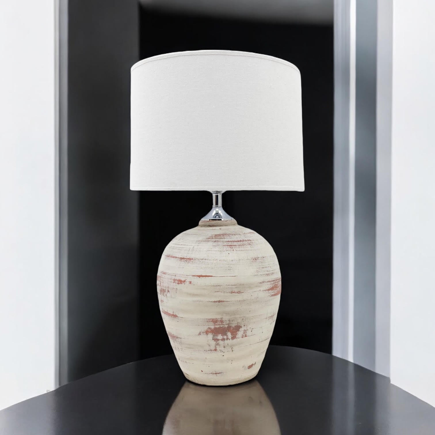 Cream ceramic table lamp with white drum shade on a dark side table