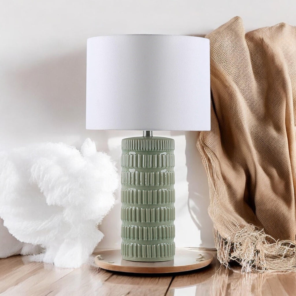 Sage green ceramic table lamp styled with neutral home textiles