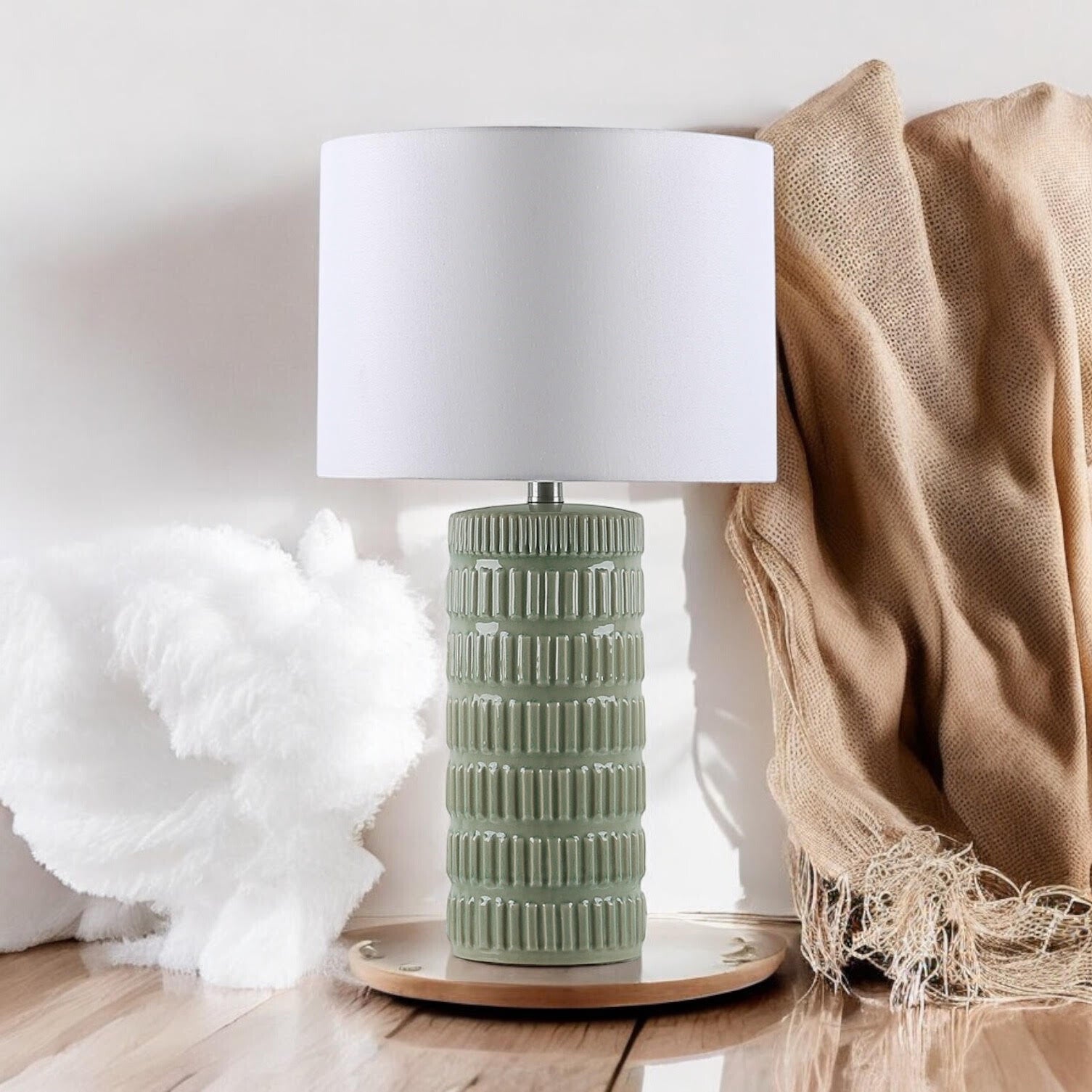 Sage green ceramic table lamp styled with neutral home textiles